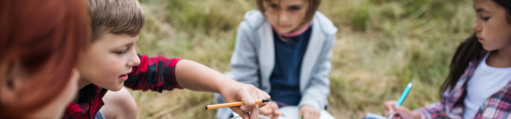 Kinder sitzen auf einer Wiese und werten ein Experiment aus