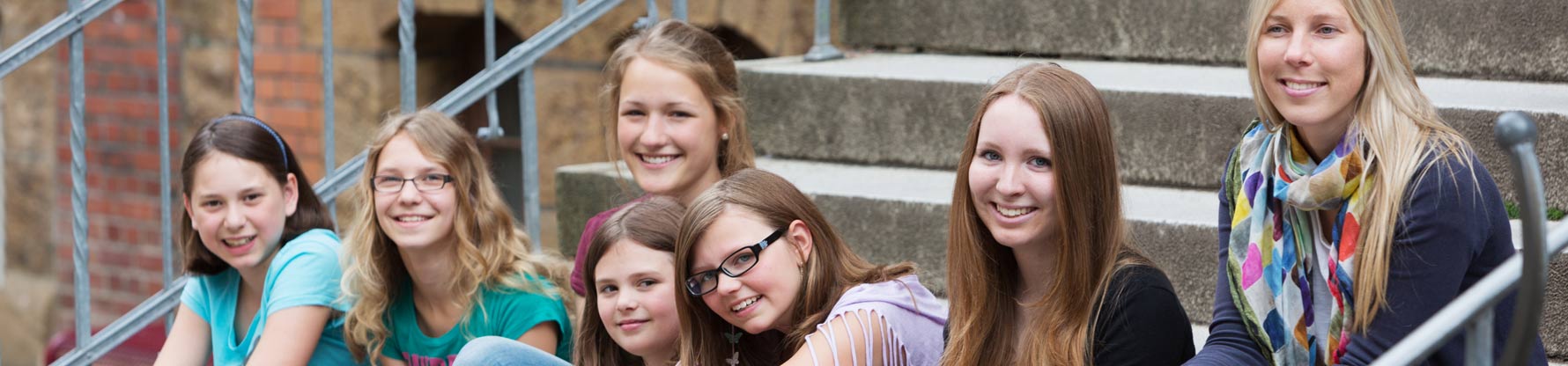 Eine Gruppe Schülerinnen sitzt im Schulhof auf einer Treppe.